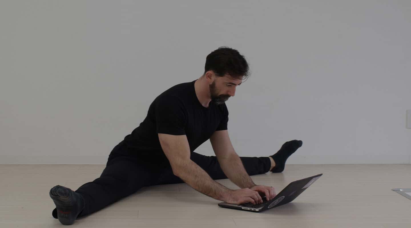 GMB Head Coach Ryan Hurst in pancake stretch working on laptop